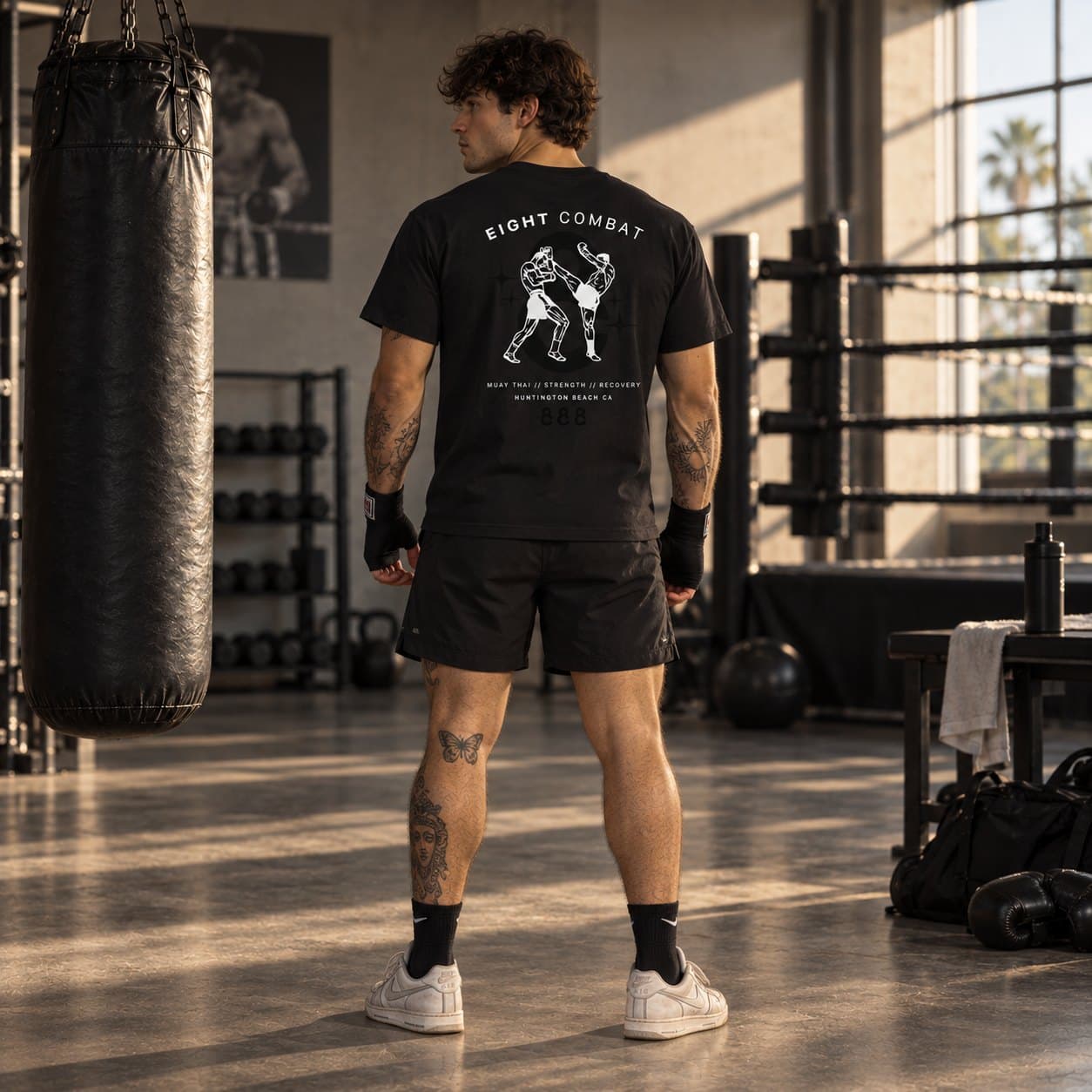 The back print of the black tee, worn, with hand wraps on, in front of the ring